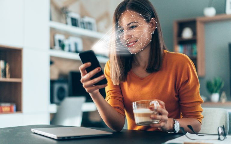 Facial recognition software scans the face of young woman holding smart phone at home