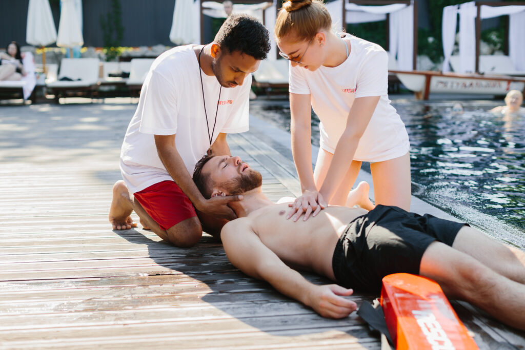 Two lifeguards performing cpr on an unconscious swimmer by the poolside, ensuring his safety and providing immediate medical assistance